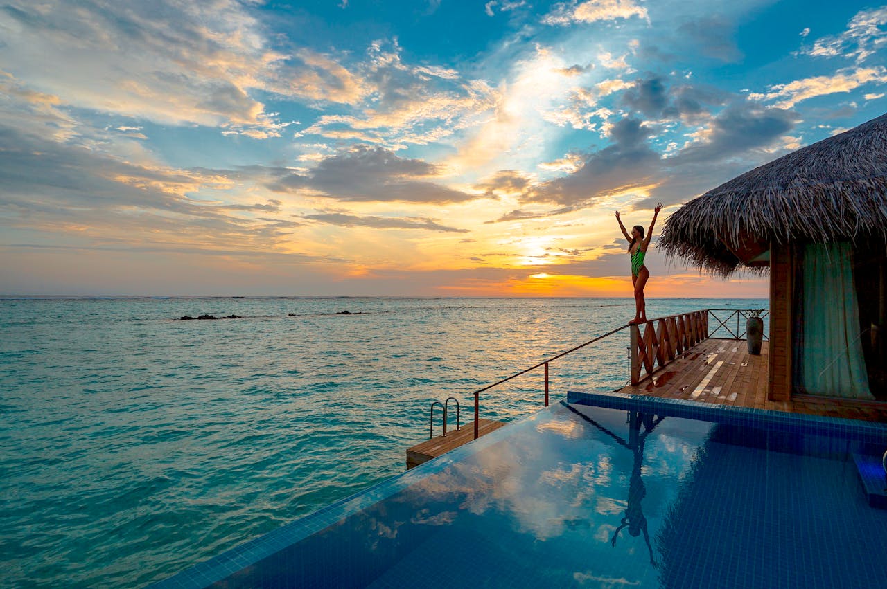 about-01 Woman enjoying a stunning sunset at a luxury Maldives resort's infinity pool.