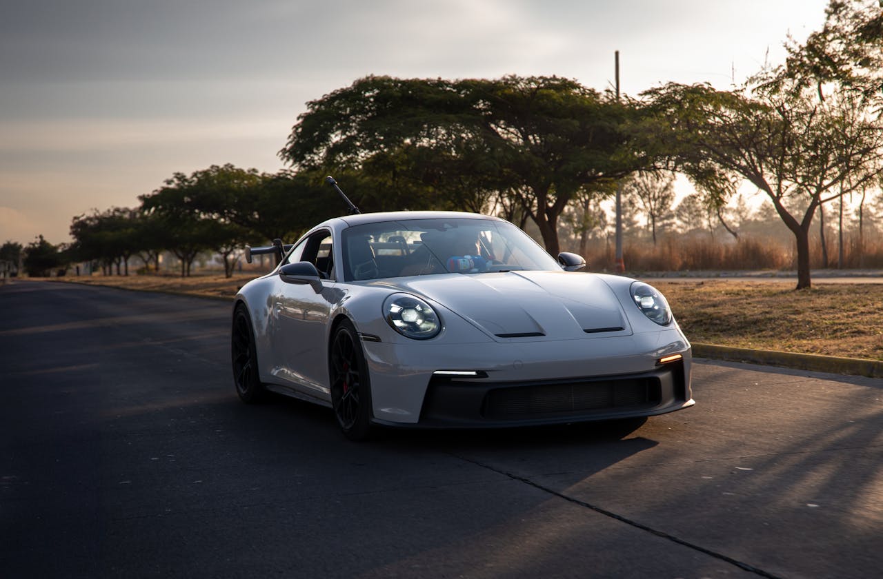 ours-journey Sleek white sports car driving on a tree-lined road in Mexico at sunset.