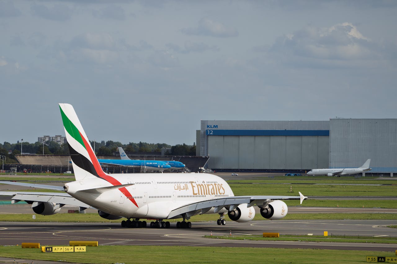 An Emirates A380 aircraft taxiing on a runway with KLM hangar in the background.